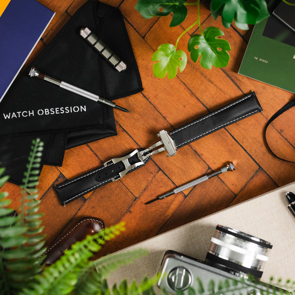 An Artem Sailcloth watch strap fitted to a clasp lay open on parquet wooden background. There are watch tools surrounding it.