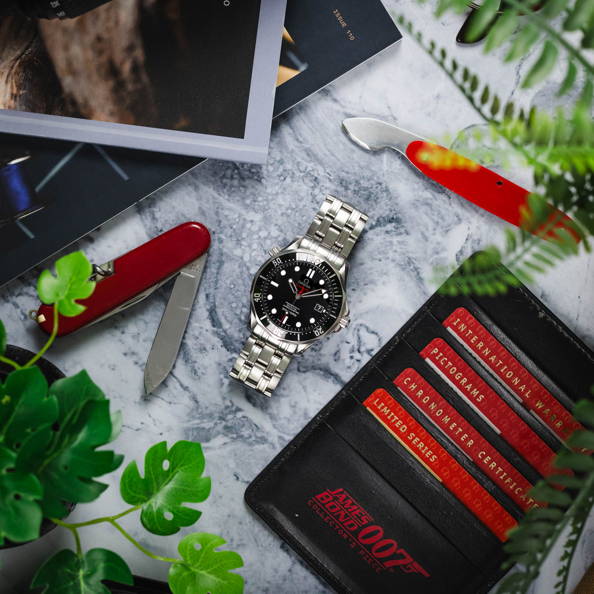 A top-down shot of an Omega Seamaster James Bond Collector's Edition watch, model 212.30.41.20.01.001, featuring a black dial with white hour markers, a date window, and red