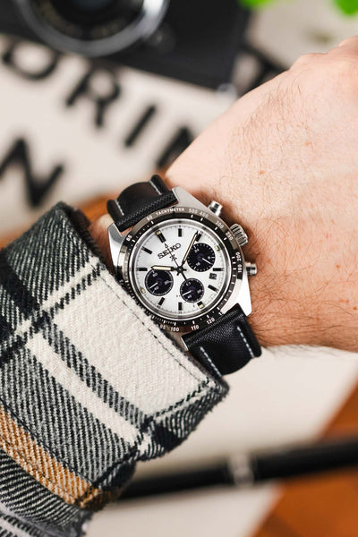 Black Artem sailcloth watch strap with grey stitching fitted to a Seiko Prospex with panda dial and silver pusher and crown, on wrist with check flannel shirt.