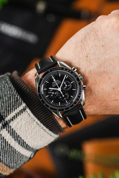 Black Artem sailcloth watch strap with white stitching fitted to a black Omega Speedmaster moonwatch and wrist with flannel check shirt.