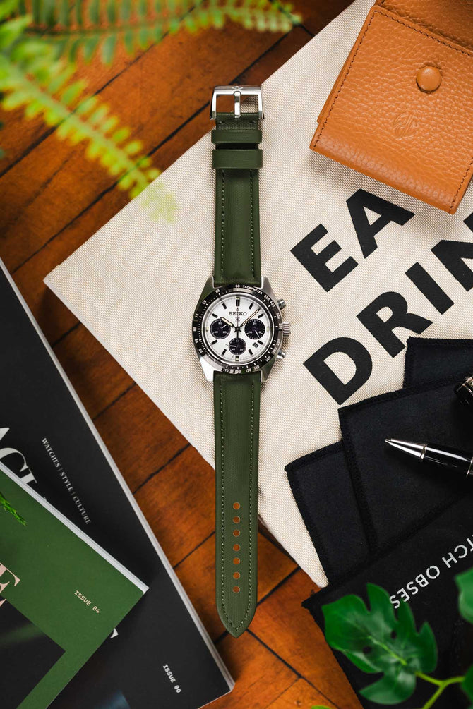 Khaki green Artem Strap Classic Sailcloth watch strap fitted to Black and White Panda Seiko chronograph Speedtimer time-piece on wooden table featuring black pen and leather watch case.