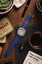 Blue Bonetto Centurini rubber strap fitted to Seiko 5 Sports Cement SRPG61K1 watch lying flat on wooden table