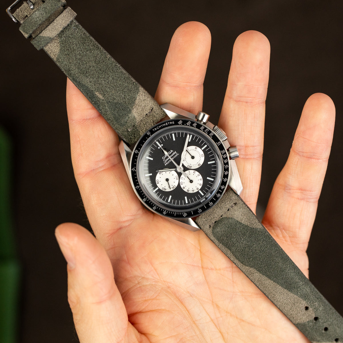 Person holding Omega Speedmaster and camouflage JPM watch strap