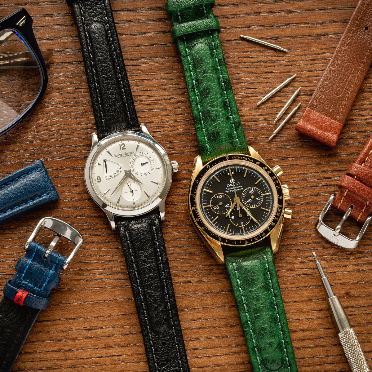 JLC and Omega watches amongst Di-modell straps on wooden desktop