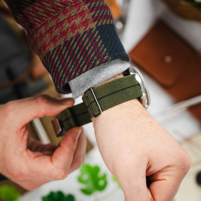 A mans wrist wearing an elasticated MN strap in green.