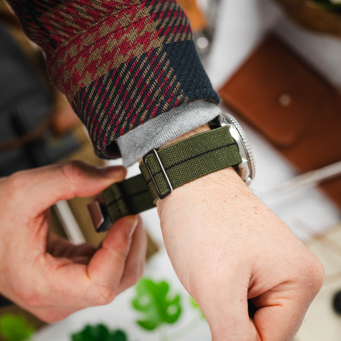 A mans wrist wearing an elasticated MN strap in green.