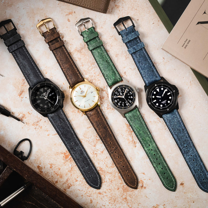 Four watches lay on a stone background, the watches are fitted to the Hirsch Stone Premium Watch Strap.