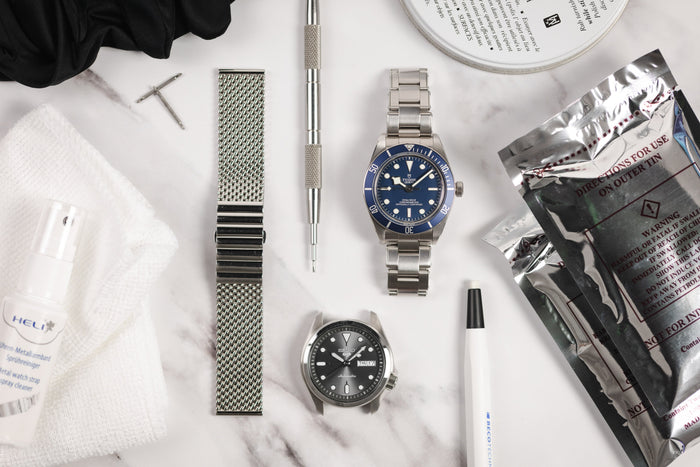 Two watches and a watch bracelet lay down surrounded by tools and polishing cloths and cleaners used to remove scratches