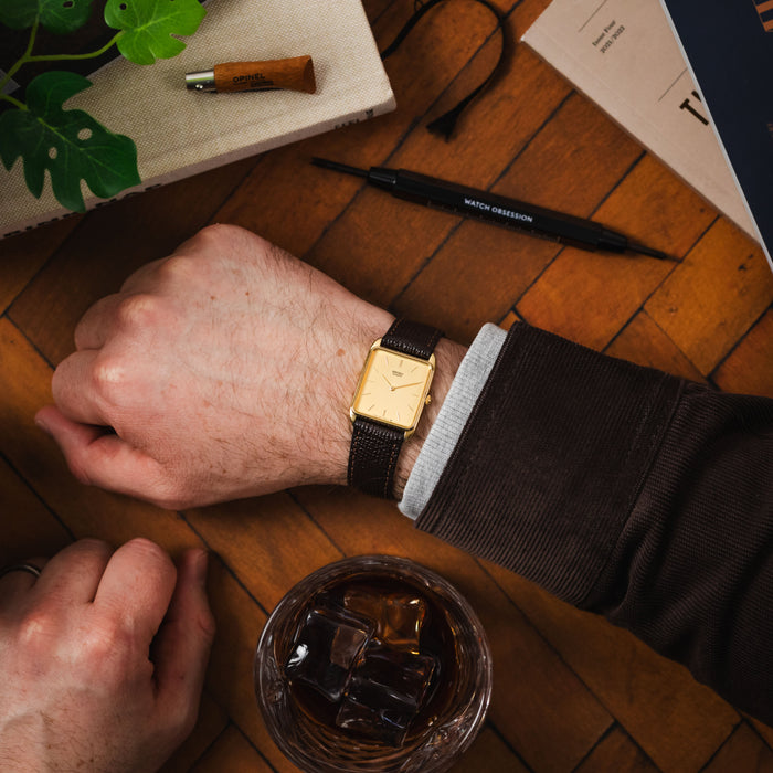 Elegant gold dress watch with a classic dark brown leather strap on a right wrist.