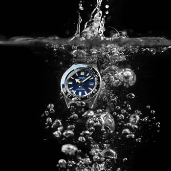 A Seiko Prospex diver's watch being dropped into water with a dramatic splash and bubbles against a black background.