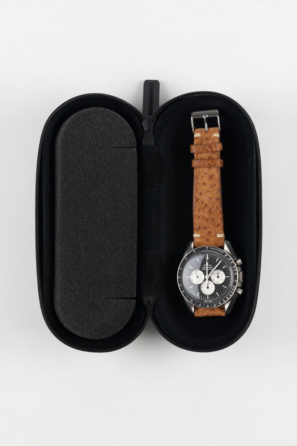 Open black hard-shell watch travel case with a foam-lined interior, displaying a wristwatch with a brown leather strap securely held in place for protection and storage.