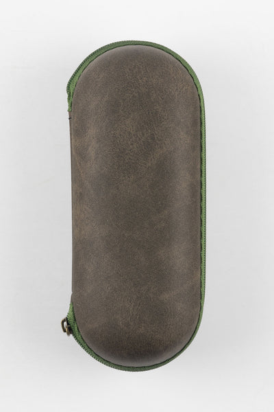 Closed oval-shaped watch travel case with a textured brown exterior and green zipper trim, shown upright against a plain light background.