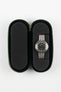 Open green zippered watch case with a black foam interior, featuring two padded compartments; a stainless steel bracelet watch with a black dial is secured in the right slot, while the left slot is empty, set against a plain light background.