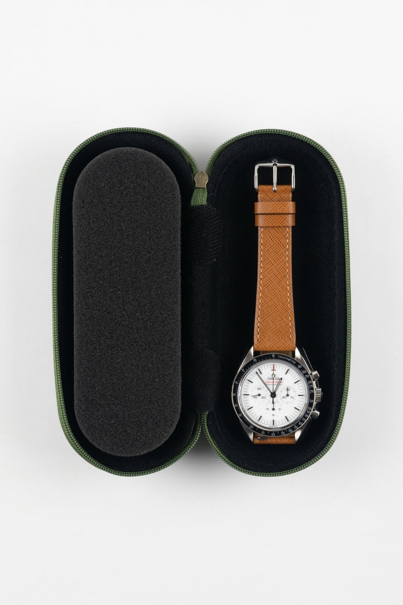 Open green zippered watch case with a black foam interior, featuring two padded compartments; a chronograph watch with a white dial, black bezel, and brown leather strap is secured in the right slot, while the left slot remains empty, set against a plain light background.