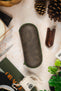 Green hard-shell watch travel case with a distressed vintage-look exterior and matching green zip-around closure, displayed on a tabletop alongside watchmaking tools and accessories.