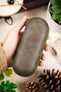 Green hard-shell watch travel case with a distressed fabric exterior and matching green zip-around closure, held in hand against a decorative tabletop background.