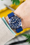 Blue Dial Tudor BB58 with Matching Blue Rubber Watch Strap on a wrist with contrasting yellow background