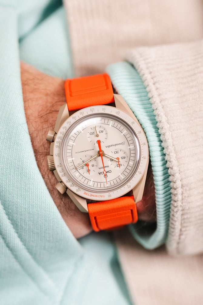 Pocket shot of a Omega X Swatch Mission to Jupiter MoonSwatch in the pocket of a turquoise hoodie and cream cord shirt, the watch is fitted to a Orange rubber strap