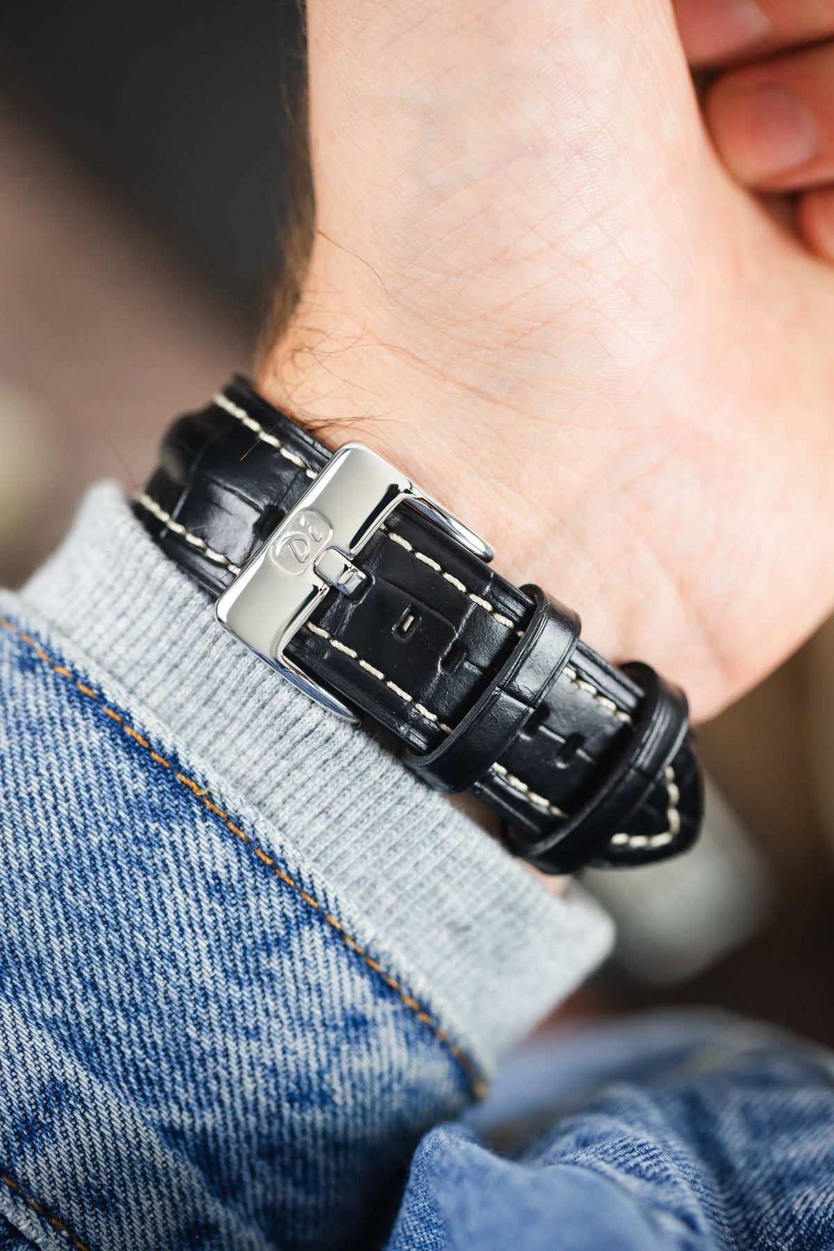 Black alligator-grain leather watch strap with cream contrast stitching and a polished stainless steel buckle, shown on wrist from the underside.