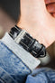 Black alligator-grain leather watch strap with cream contrast stitching and a polished stainless steel buckle, shown on wrist from the underside.