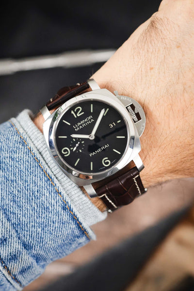 Panerai Luminor Marina on a dark brown alligator-grain leather strap with cream contrast stitching, shown on wrist with a black dial and signature crown guard.