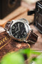 Panerai Luminor Marina on a dark brown alligator-grain leather strap with cream contrast stitching, displayed on a vintage wooden box with retro camera accessories.