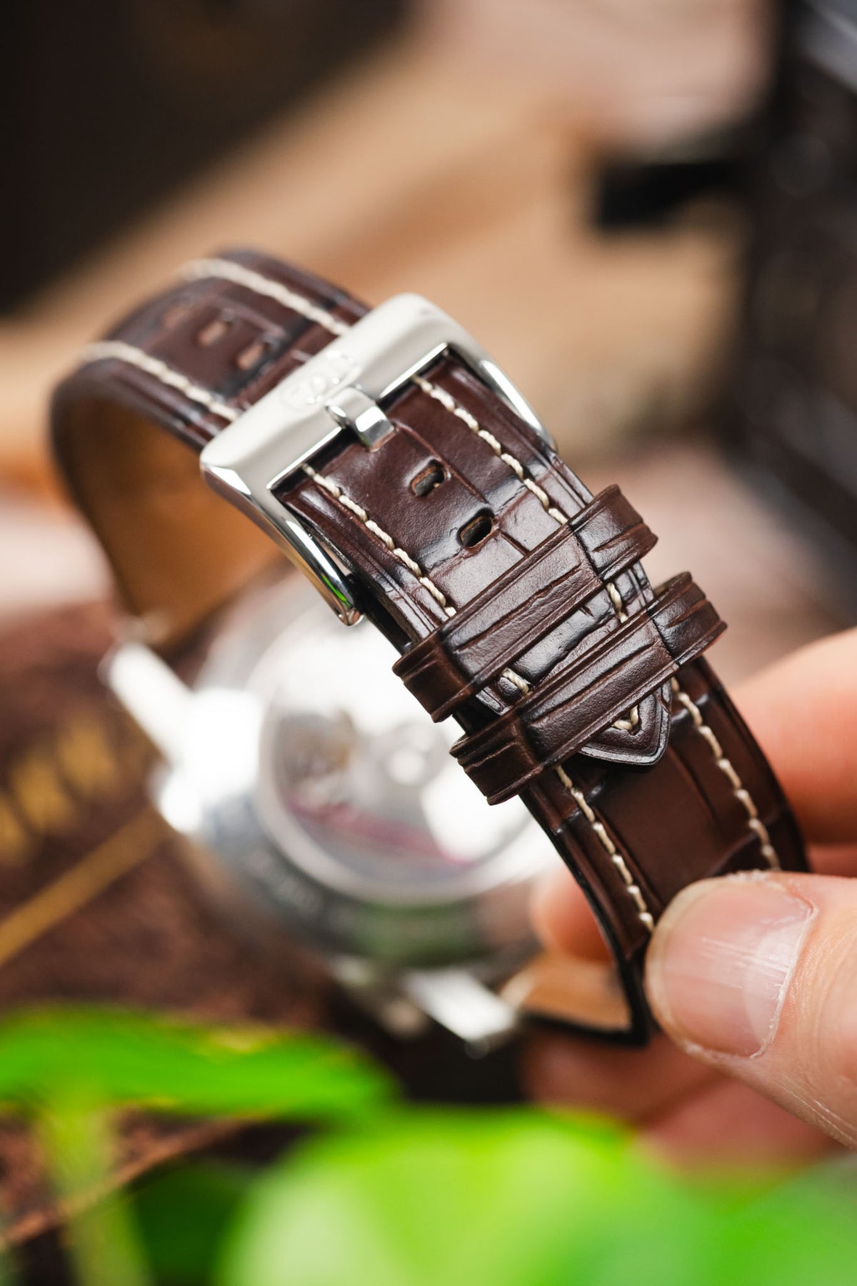 Dark brown alligator-grain leather watch strap with cream contrast stitching and a polished stainless steel buckle, shown in a close-up detail shot.
