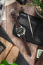Panerai Luminor Marina on a dark brown alligator-grain leather strap with cream contrast stitching, displayed on a leather pouch with watchmaking tools and vintage accessories.