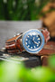 Unimatic dive watch on a gold brown alligator-grain leather strap with cream contrast stitching, displayed on vintage camera equipment with a blue dial and bezel.