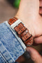 Gold brown alligator-grain leather watch strap with cream contrast stitching and a polished stainless steel buckle, shown on wrist from the underside.