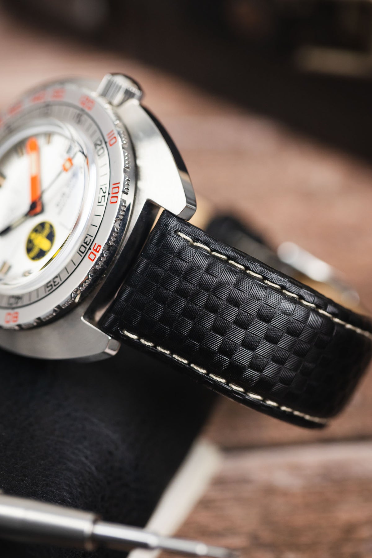Black carbon-fibre-pattern leather watch strap with white contrast stitching, fitted to a Doxa dive watch in a close-up detail shot.