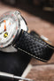 Black carbon-fibre-pattern leather watch strap with white contrast stitching, fitted to a Doxa dive watch in a close-up detail shot.