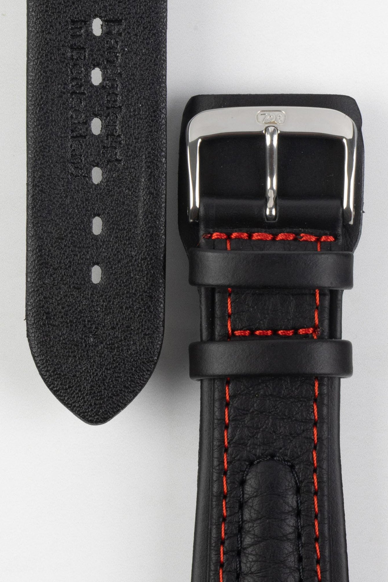 Close-up detail view of a black padded leather rally-style watch strap featuring contrasting red stitching, integrated lug-end reinforcement panels, dual keeper loops, a polished stainless steel buckle, and a textured black leather lining with embossed branding, displayed on a light grey background to highlight the premium handcrafted construction, cushioned profile, and motorsport-inspired design.