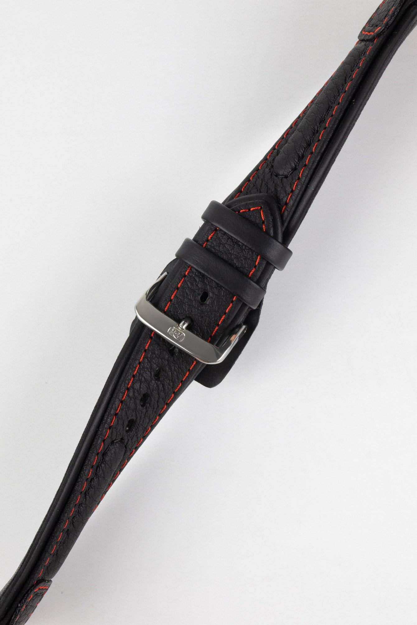 Close-up of a black padded leather rally-style watch strap with contrasting red stitching, dual keeper loops, multiple adjustment holes, and a polished stainless steel buckle, displayed diagonally on a light grey background to highlight the supple leather texture, tapered profile, cushioned construction, and motorsport-inspired design.