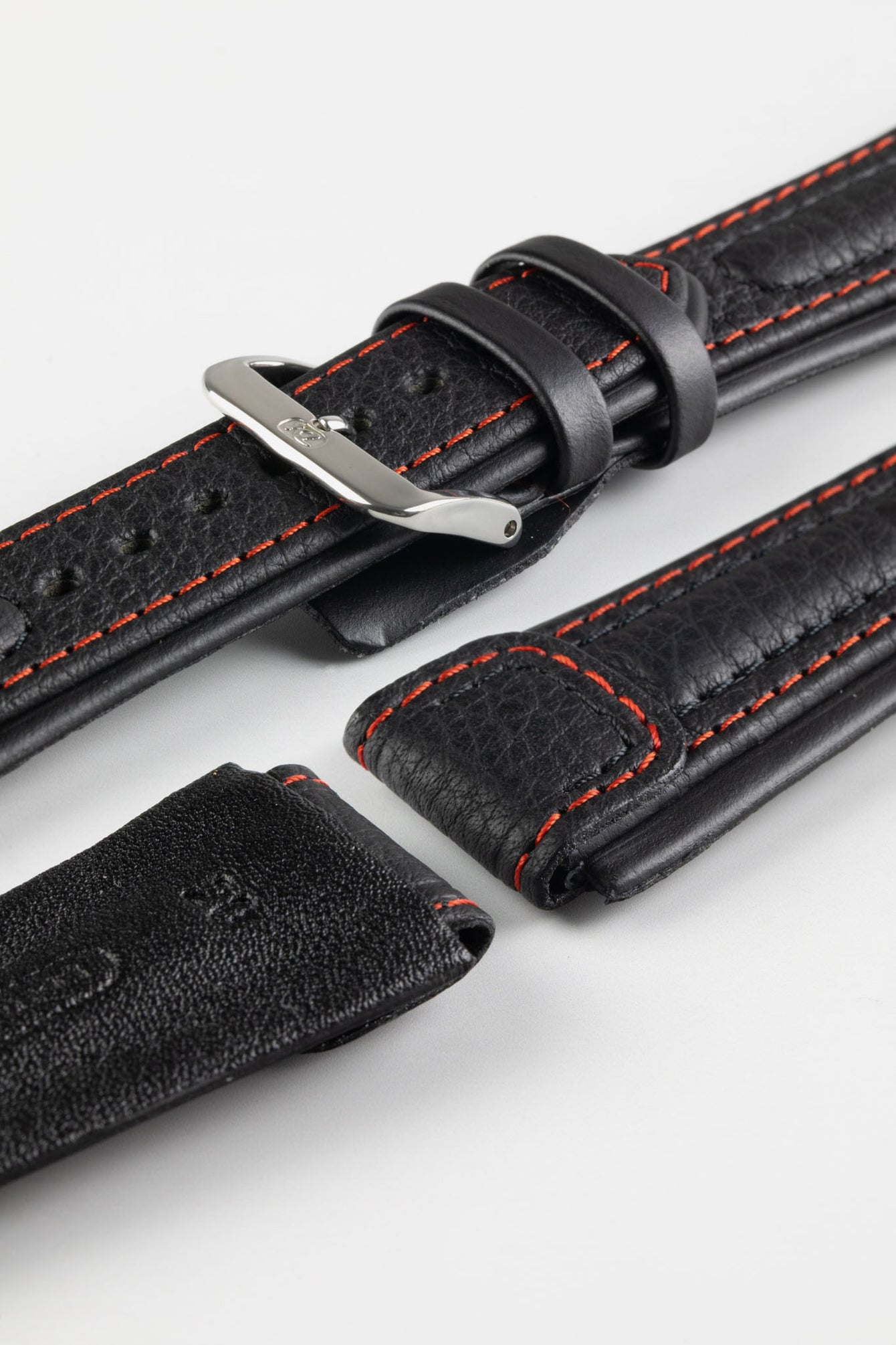 Close-up detail of a black padded leather rally-style watch strap featuring contrasting red stitching, integrated lug-end reinforcement panels, dual keeper loops, multiple adjustment holes, a polished stainless steel buckle, and a black leather lining, displayed on a light grey background to highlight the supple leather texture, cushioned construction, and motorsport-inspired design.