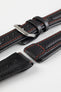 Close-up detail of a black padded leather rally-style watch strap featuring contrasting red stitching, integrated lug-end reinforcement panels, dual keeper loops, multiple adjustment holes, a polished stainless steel buckle, and a black leather lining, displayed on a light grey background to highlight the supple leather texture, cushioned construction, and motorsport-inspired design.