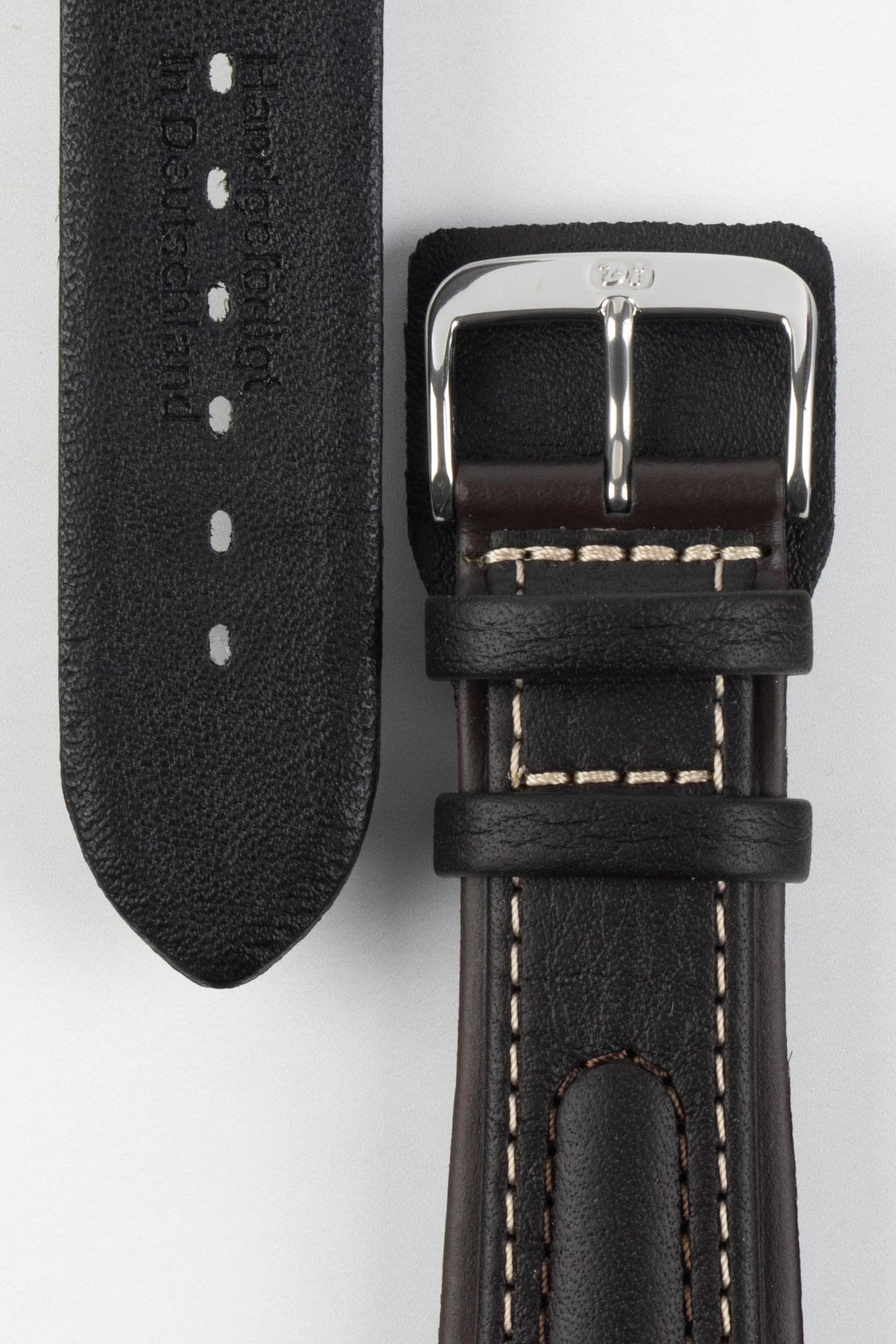 Close-up detail view of a dark brown padded leather rally-style watch strap featuring cream contrast stitching, integrated lug-end reinforcement panels, dual keeper loops, a polished stainless steel buckle, and a black textured leather lining embossed with manufacturer branding, displayed on a light grey background to highlight the premium handcrafted construction, cushioned profile, and vintage motorsport-inspired design.