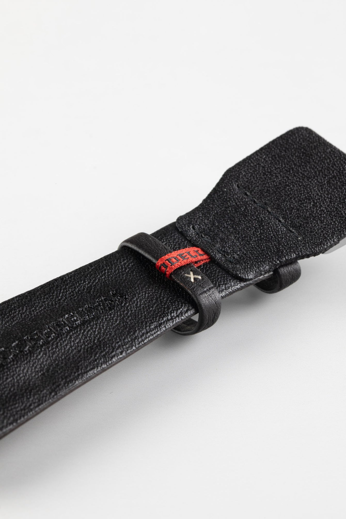 Close-up of the underside of a dark brown padded leather rally-style watch strap, featuring a black textured leather lining with embossed branding, dual black leather keeper loops, a distinctive red woven accent keeper, and reinforced lug-end padding, displayed on a light grey background to highlight the premium handcrafted construction, contrasting details, and vintage motorsport-inspired design.
