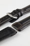 Close-up detail view of a dark brown padded leather rally-style watch strap featuring cream contrast stitching, a polished stainless steel buckle, dual keeper loops, integrated lug-end reinforcement panels, and a black leather lining with embossed branding, displayed on a light grey background with one strap section detached to highlight the premium handcrafted construction, cushioned profile, and vintage motorsport-inspired design.