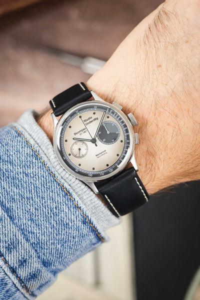 Studio Underd0g Bicompax chronograph watch on a black leather strap with beige contrast stitching, shown on wrist with a beige dial and stainless steel case.