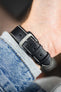 Black leather watch strap with beige contrast stitching and a polished stainless steel buckle, shown on wrist from the underside.