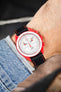 Omega x Swatch MoonSwatch chronograph on a black leather strap with red contrast stitching, shown on wrist with a red case and white dial.