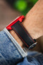 Black leather watch strap with red contrast stitching and a polished stainless steel buckle, shown on wrist with a red Omega x Swatch MoonSwatch chronograph.