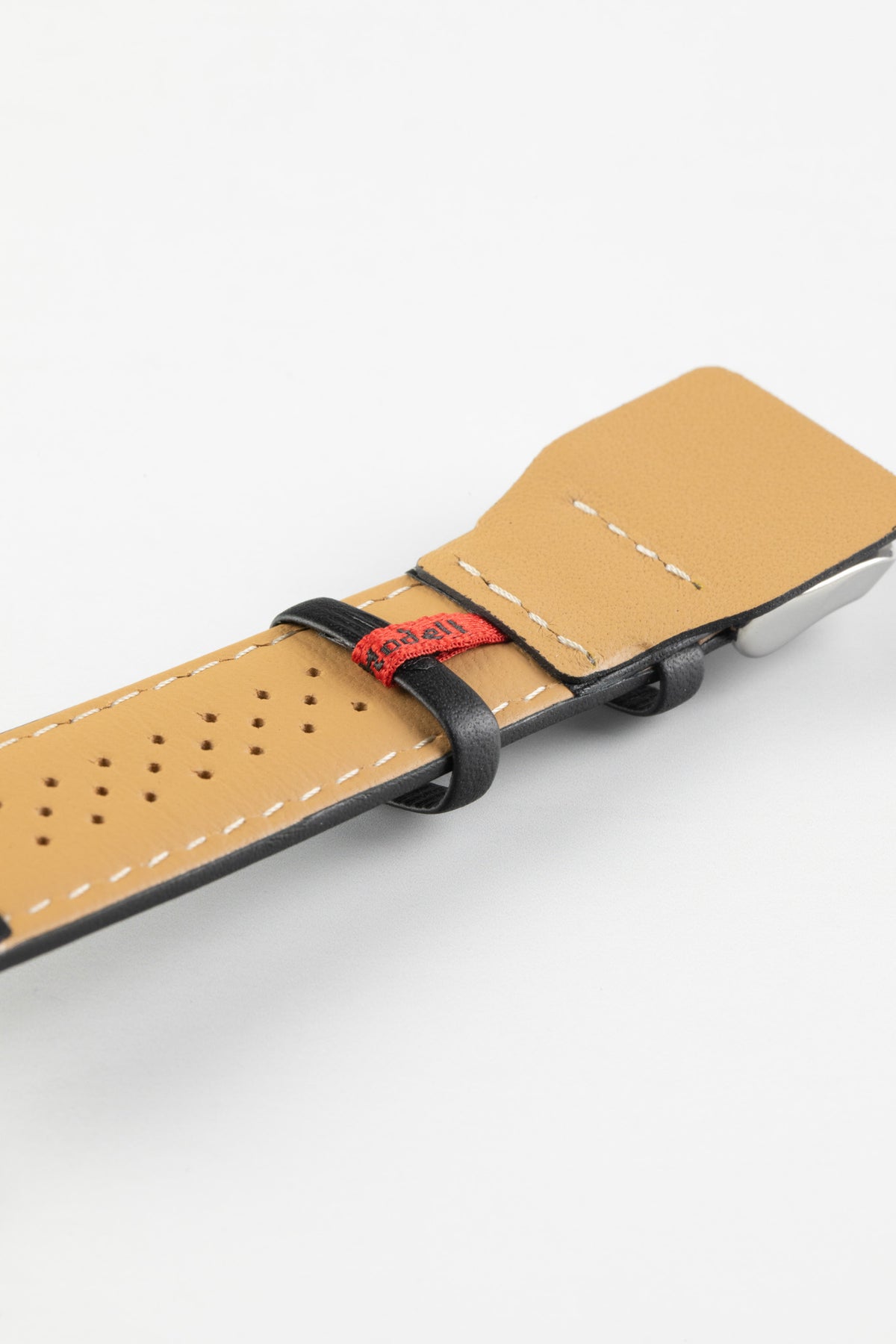 Black leather watch strap with a beige perforated leather lining, white stitching, and a polished stainless steel buckle, shown in close-up on a white background.