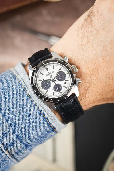 Seiko Speedtimer chronograph on a black alligator-grain leather strap, shown on wrist with a white panda dial and black tachymeter bezel.