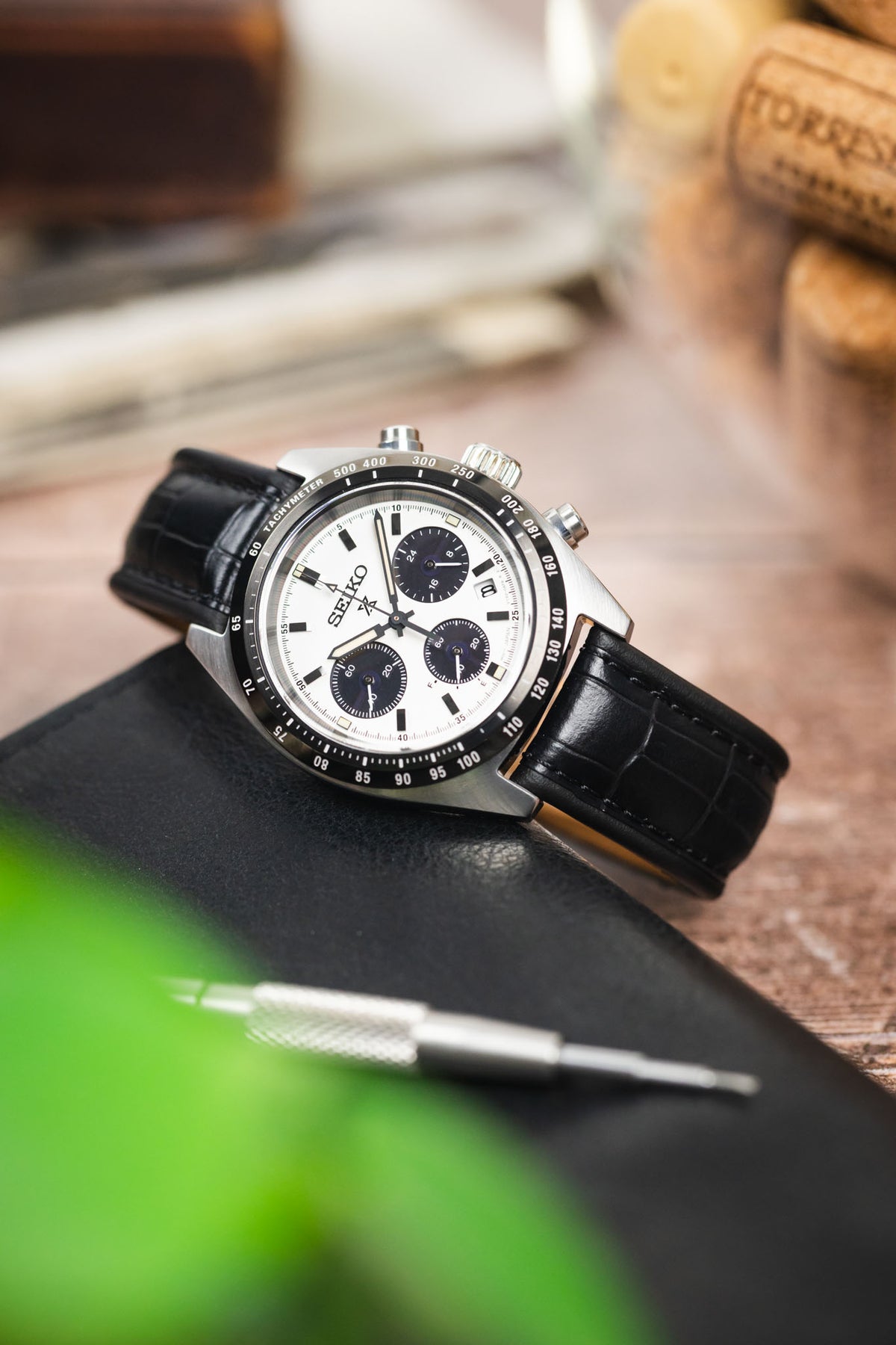 Seiko Speedtimer chronograph on a black alligator-grain leather strap, displayed on a leather pouch with watchmaking tools and vintage accessories.