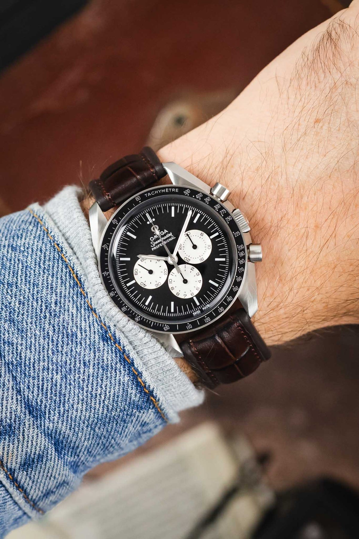 Omega Speedmaster Professional chronograph on a dark brown alligator-grain leather strap, shown on wrist with a black dial and tachymeter bezel.