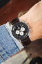 Omega Speedmaster Professional chronograph on a dark brown alligator-grain leather strap, shown on wrist with a black dial and tachymeter bezel.