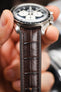 Dark brown alligator-grain leather watch strap fitted to an Omega Speedmaster Professional, highlighting the embossed crocodile pattern and rich brown finish.