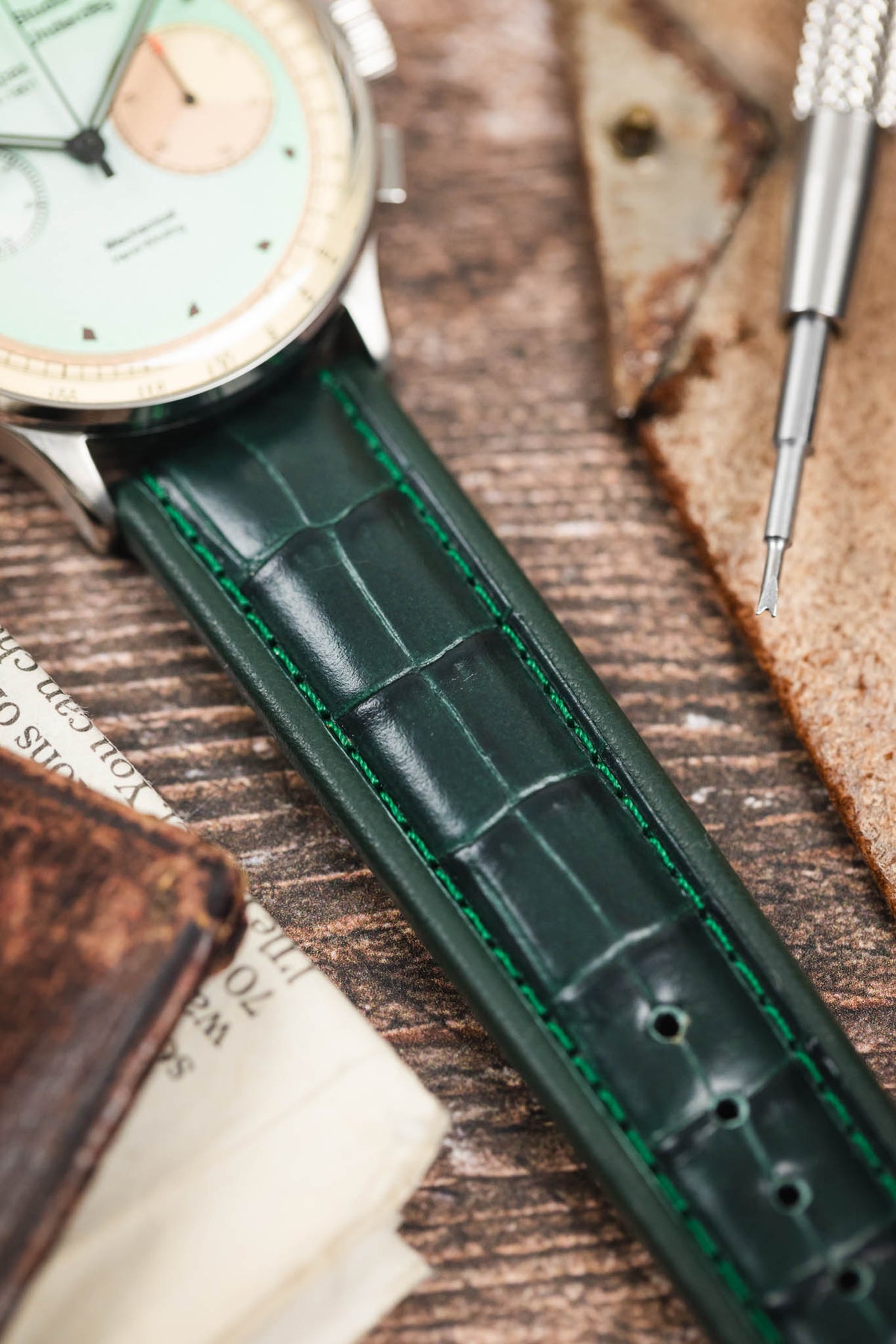 Dark green alligator-grain leather watch strap with green contrast stitching, fitted to a Studio Underd0g Bicompax chronograph watch in a close-up detail shot.